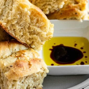 Squares of black pepper focaccia bread on a plate next to a bowl of olive oil and balsamic vinegar.