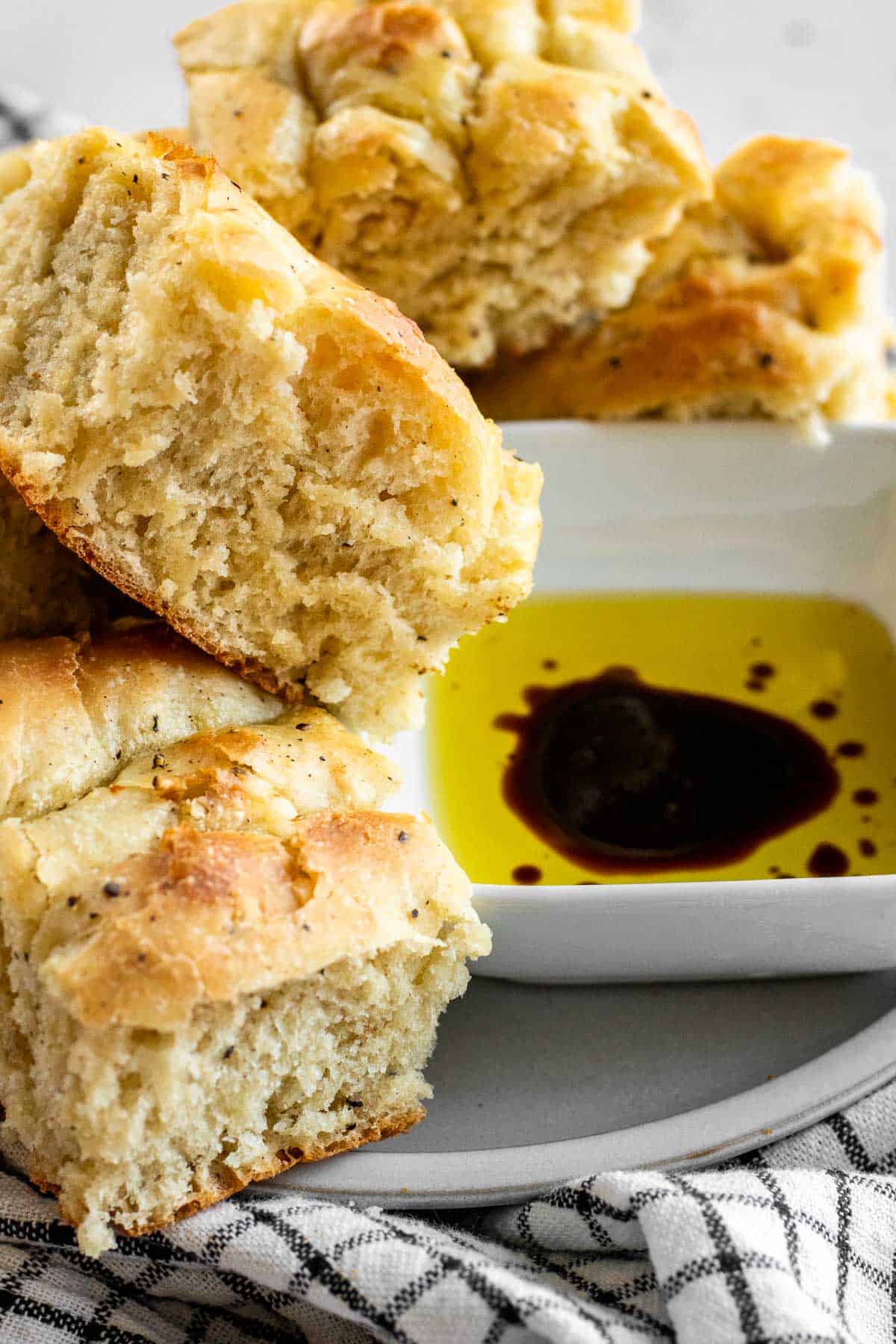 Squares of black pepper focaccia bread on a plate next to a bowl of olive oil and balsamic vinegar.