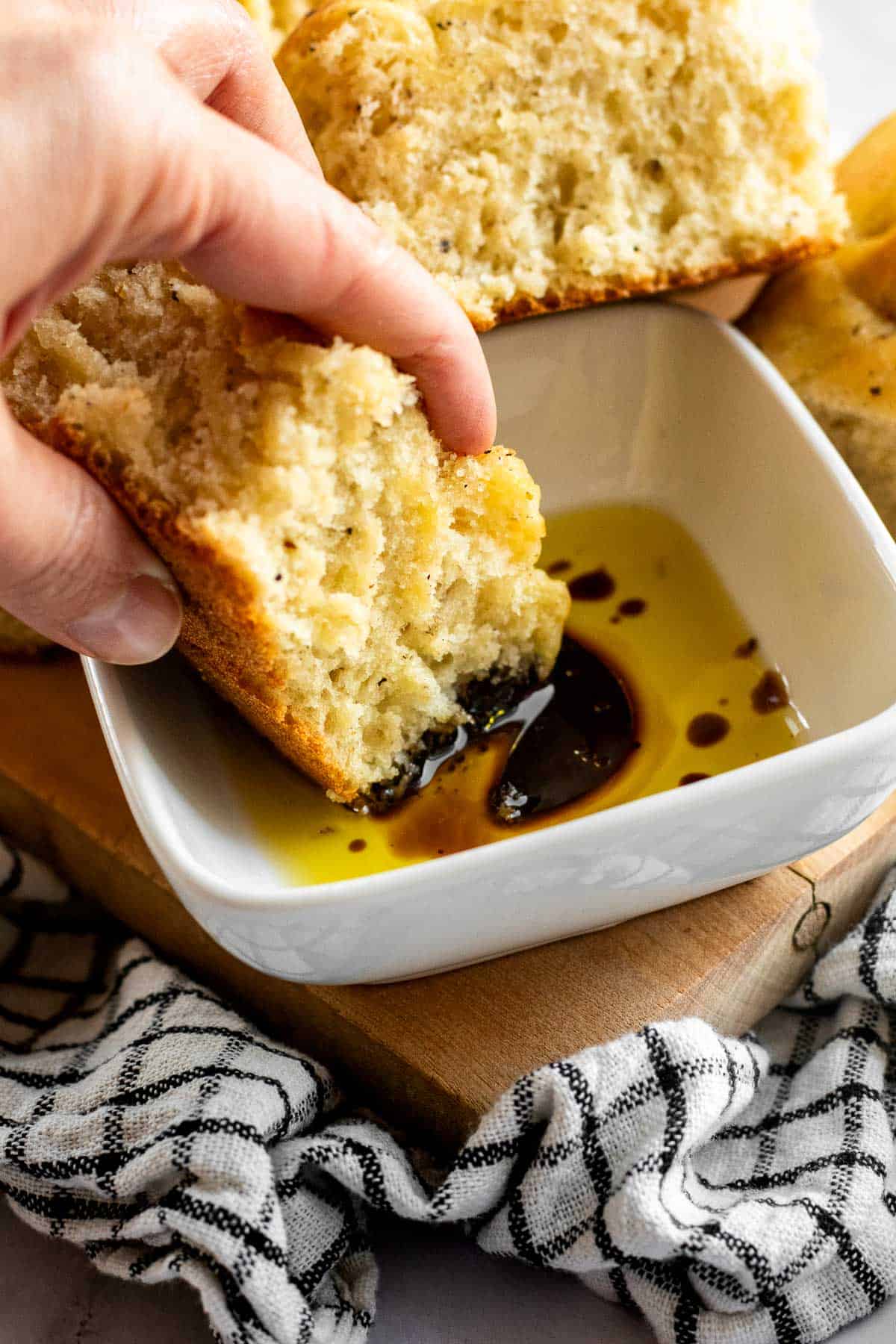 A hand dipping a square of focaccia bread into a bowl of olive oil and balsamic vinegar.