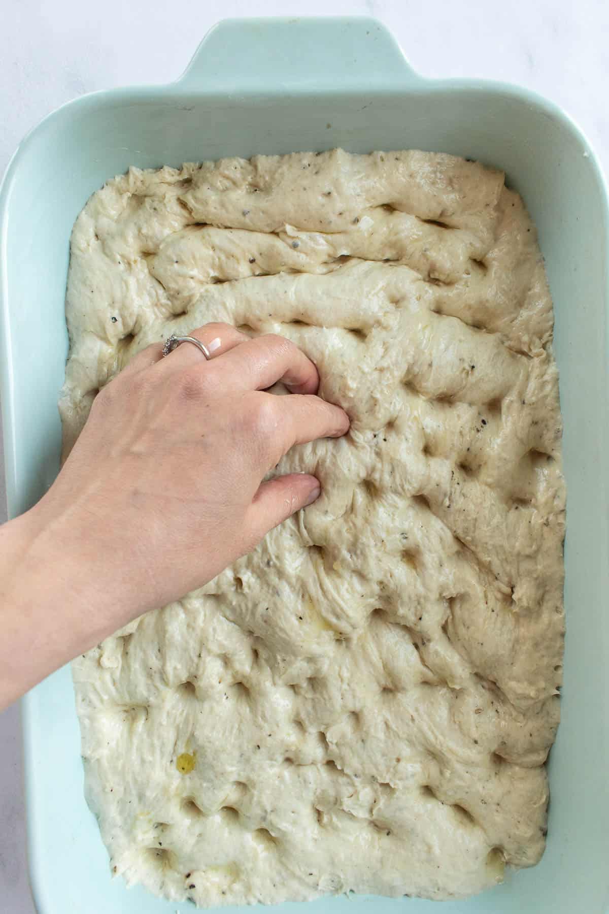 A hand dimpling focaccia dough in a large baking dish.