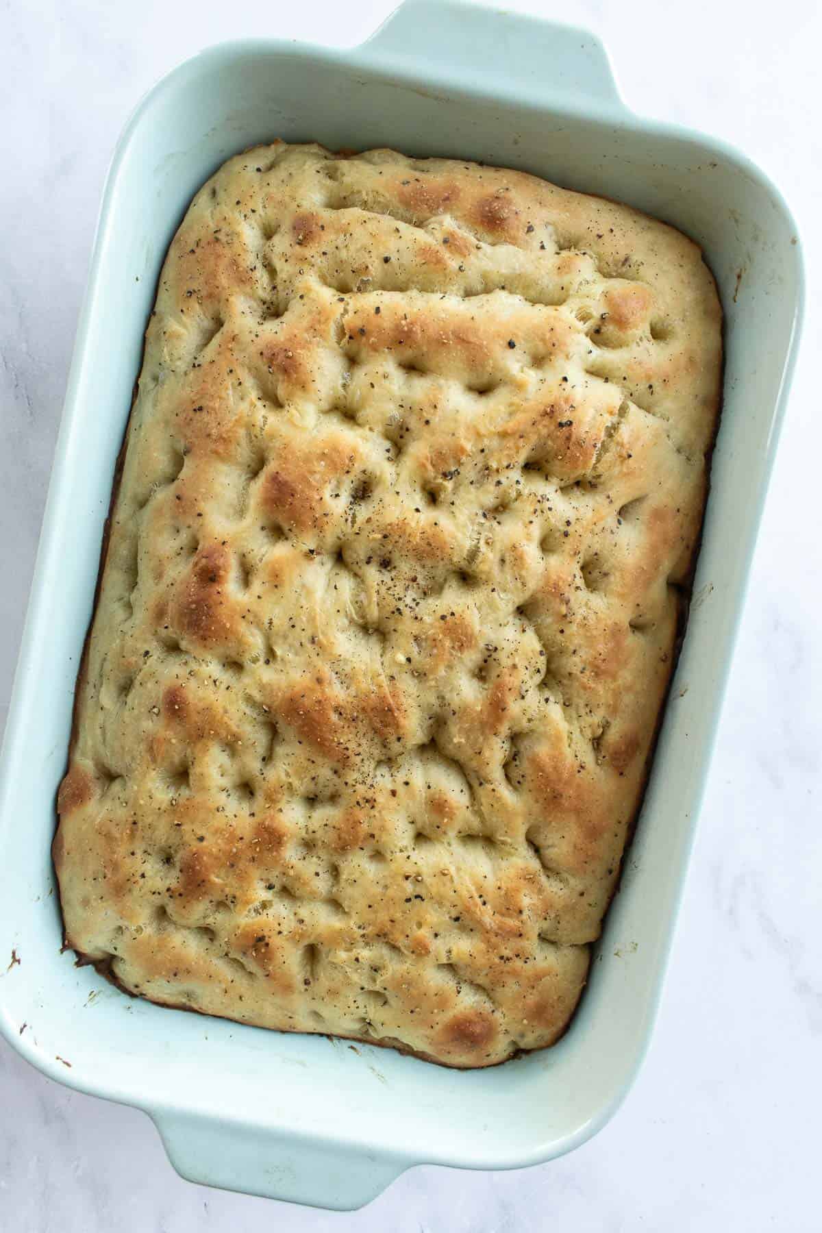 Baked black pepper focaccia bread in a large blue baking dish.