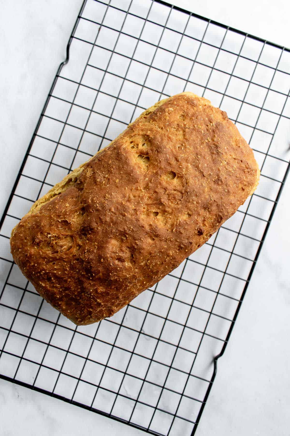 A baked loaf of golden brown sandwich bread on a wire cooling rack.