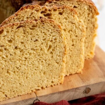 Two slices of light brown sandwich bread next to the rest of the loaf on a wooden board.