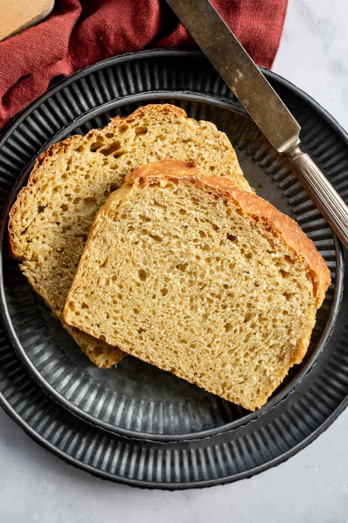 Two slices of golden sandwich bread on stacked metal plates with a butter knife.