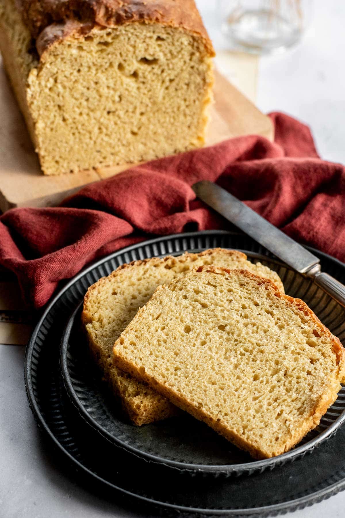 Two slices of golden sandwich bread on a metal plate next to the rest of the loaf on a cutting board.