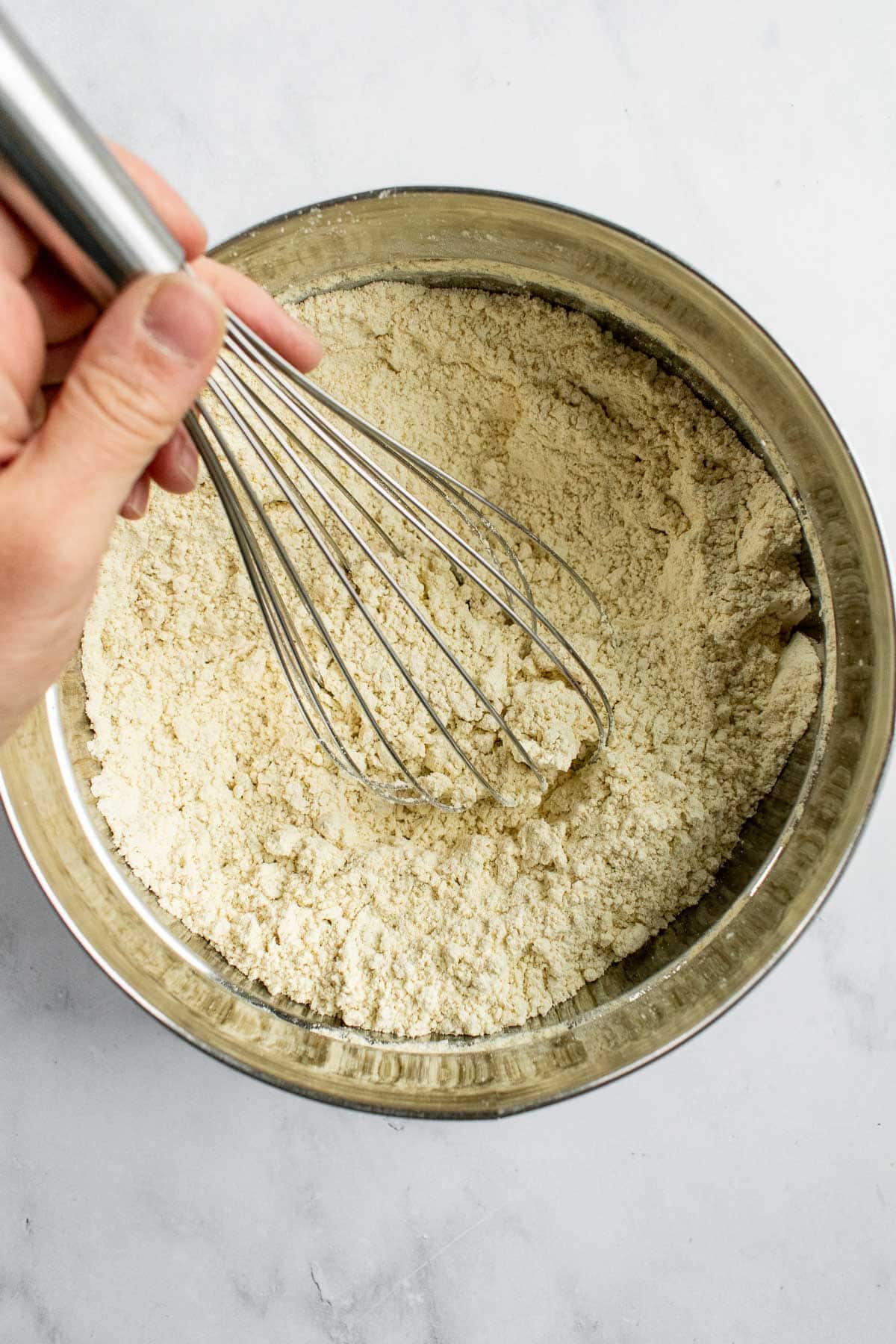 A hand whisking flour, salt, and yeast in a mixing bowl.