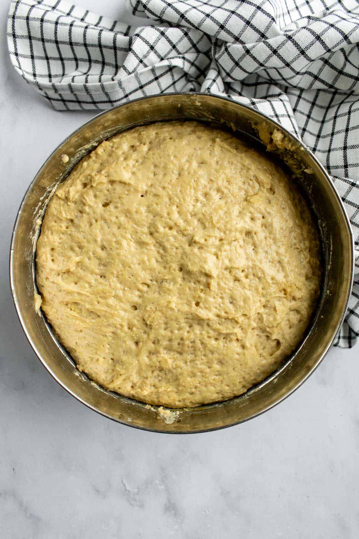 A metal bowl filled with bubbly, risen bread dough on a light surface.
