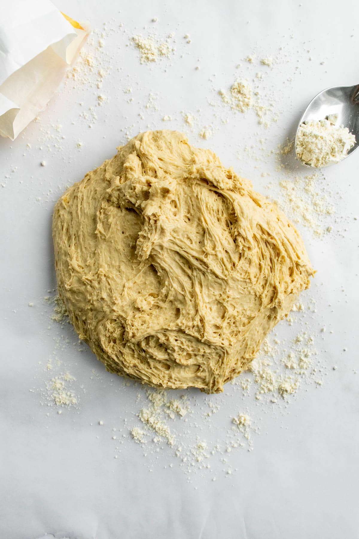 A sticky, soft bread dough on a floured marble surface.