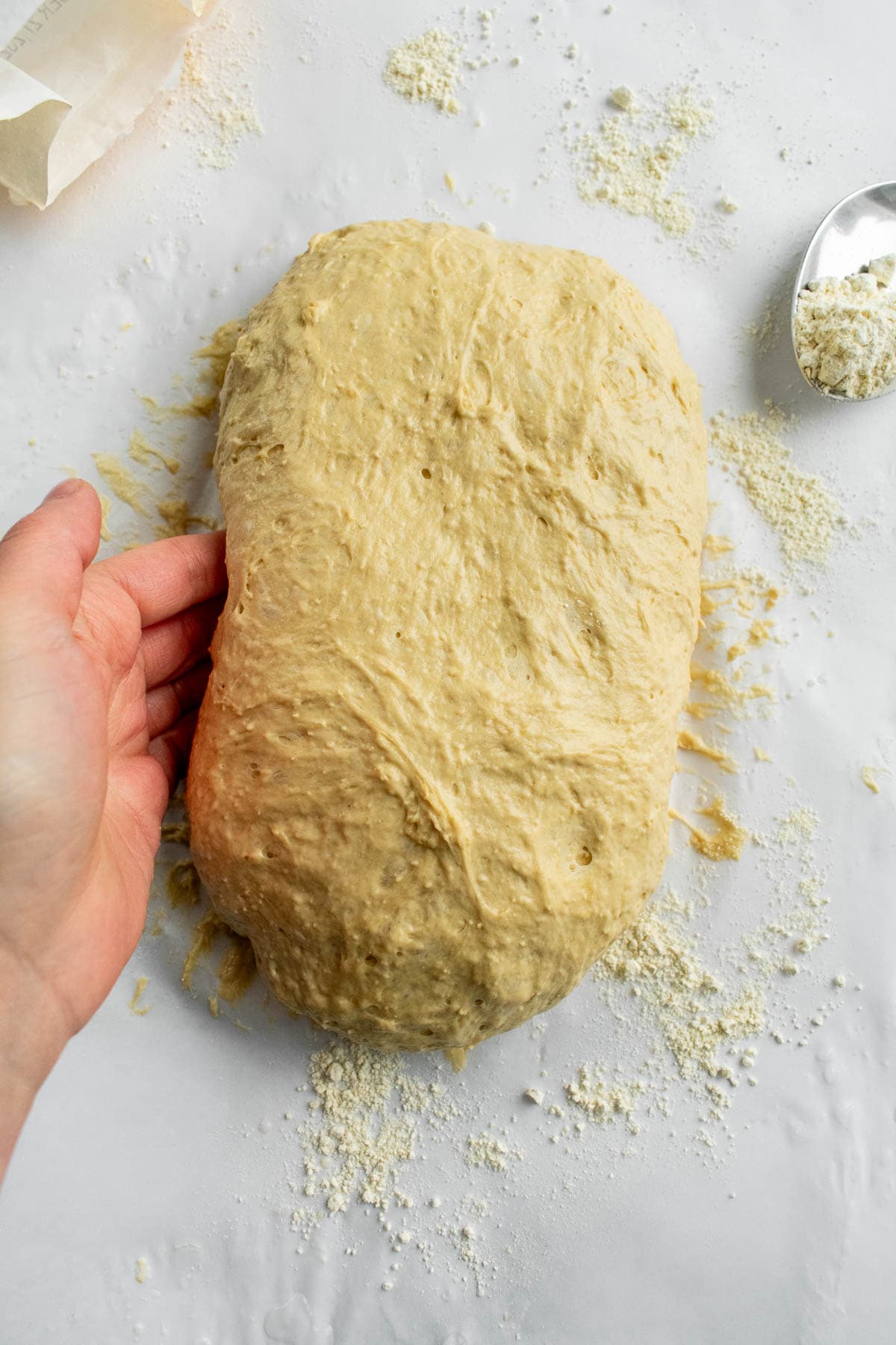 A hand shaping light bread dough into an oval on a lightly floured surface.