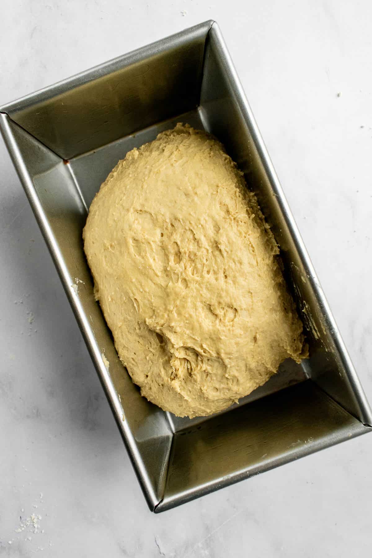 A metal loaf pan half-filled with a light beige bread dough.