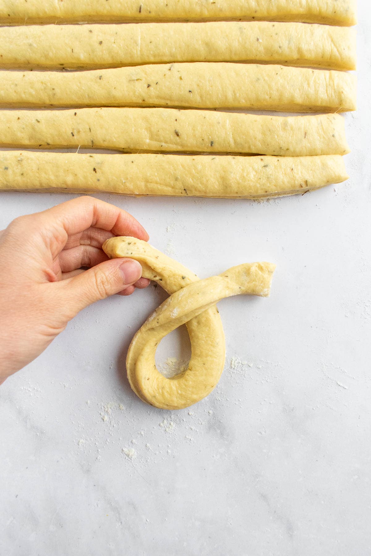 A hand pulling a strip of soft bread dough into a loop on a light surface.