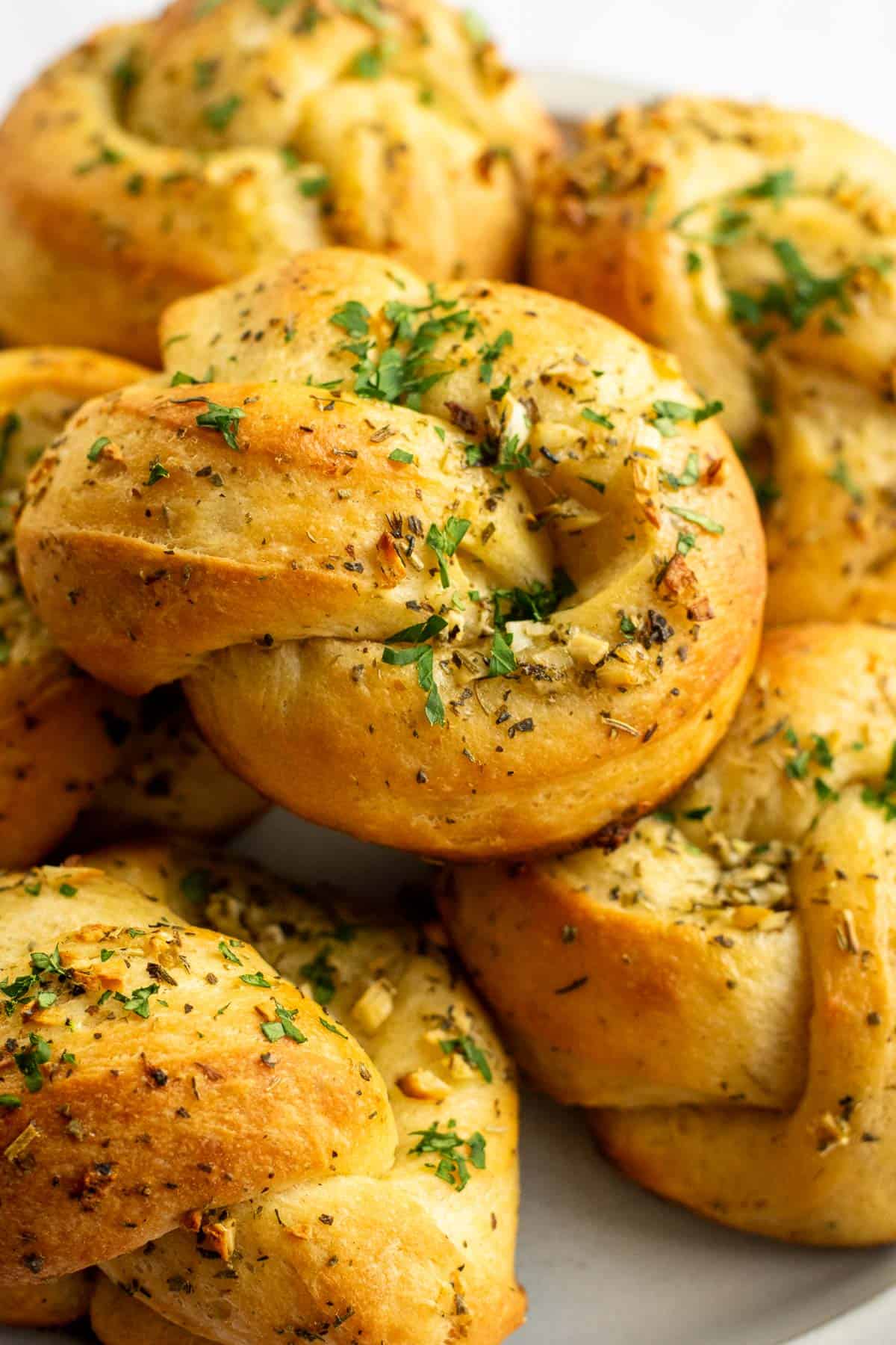 Half a dozen garlic knots topped with chopped green herbs piled on a grey plate.