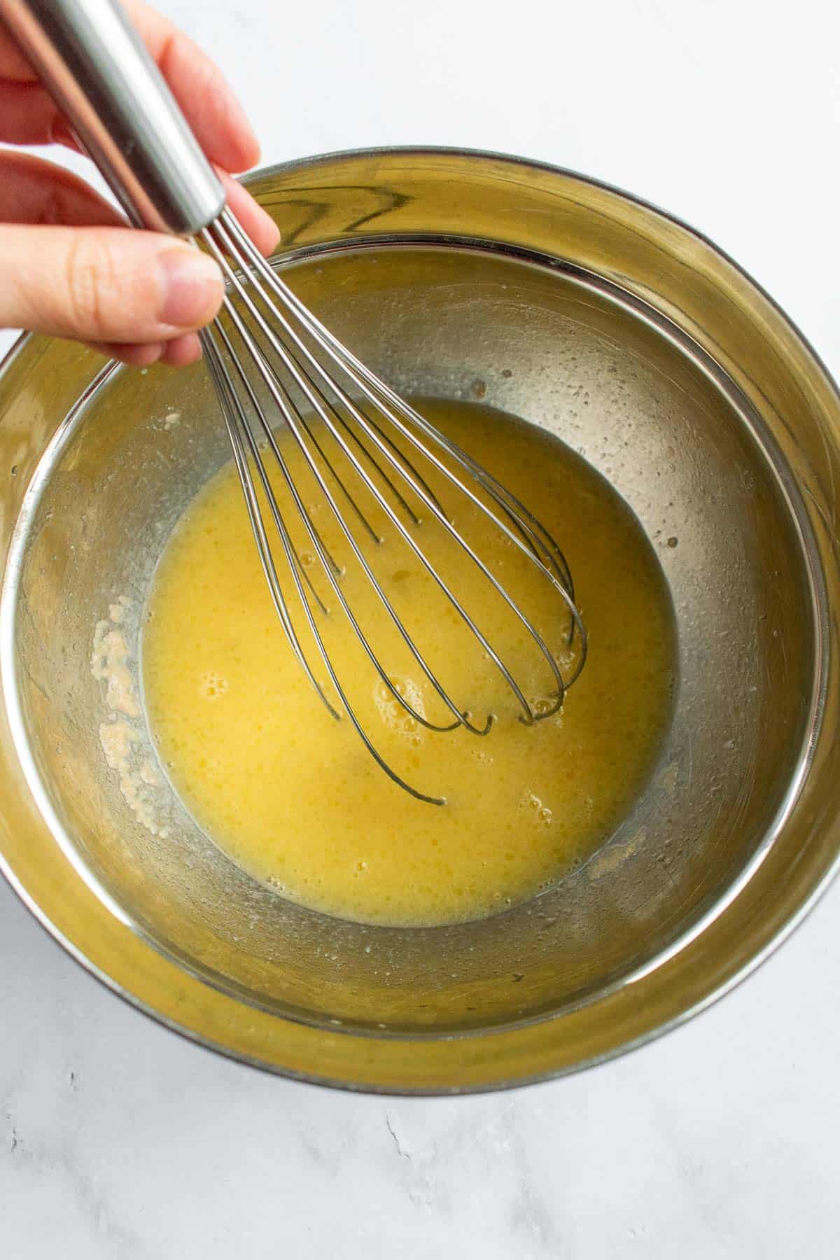 A hand whisking melted butter in a metal mixing bowl.