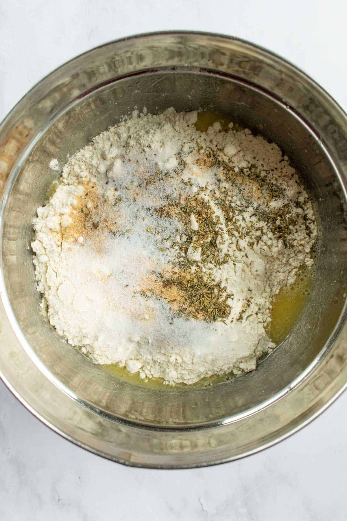 Flour, salt, garlic powder, and dried herbs in a metal mixing bowl.