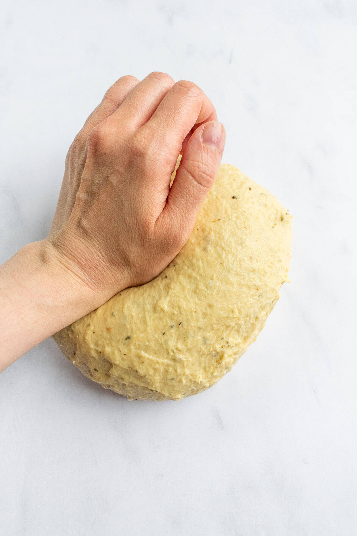 A hand kneading enriched bread dough on a light surface.