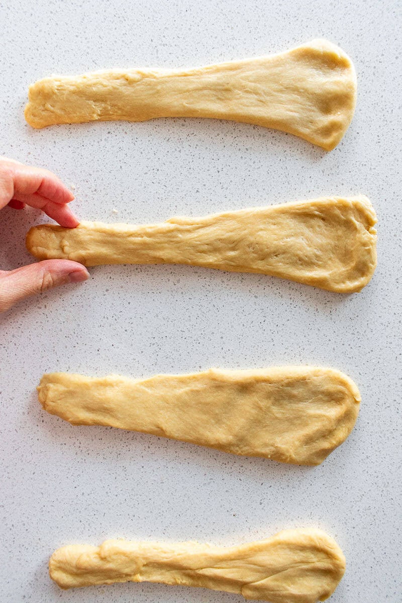A hand shaping soft bread dough into flat, long cones on a counter.