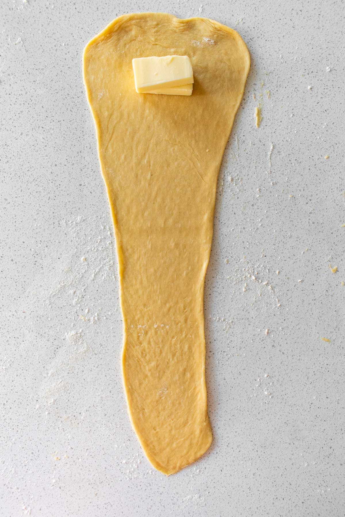 A long, flat cone of bread dough with a small block of butter near the top of the wide end.