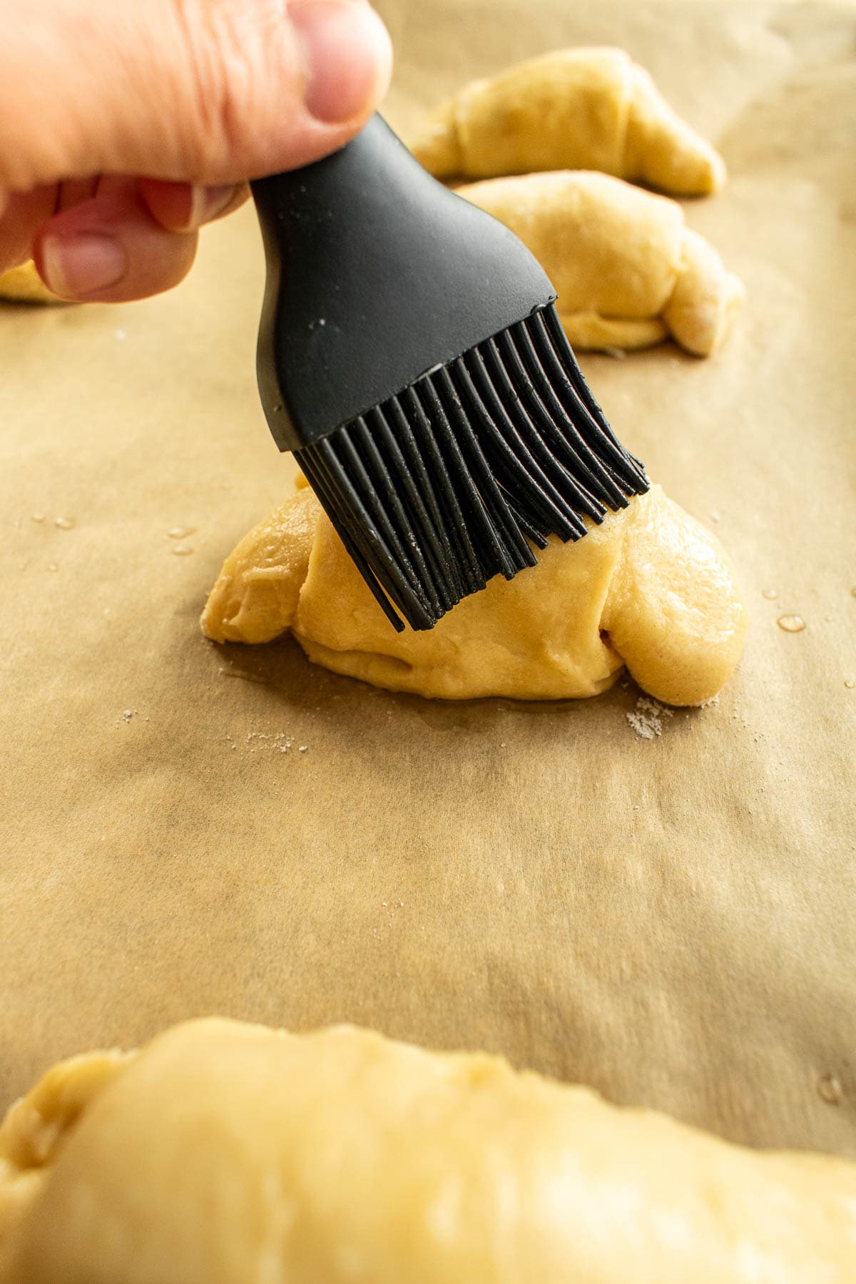 A hand brushing water onto a dough bun with a silicone pastry brush.