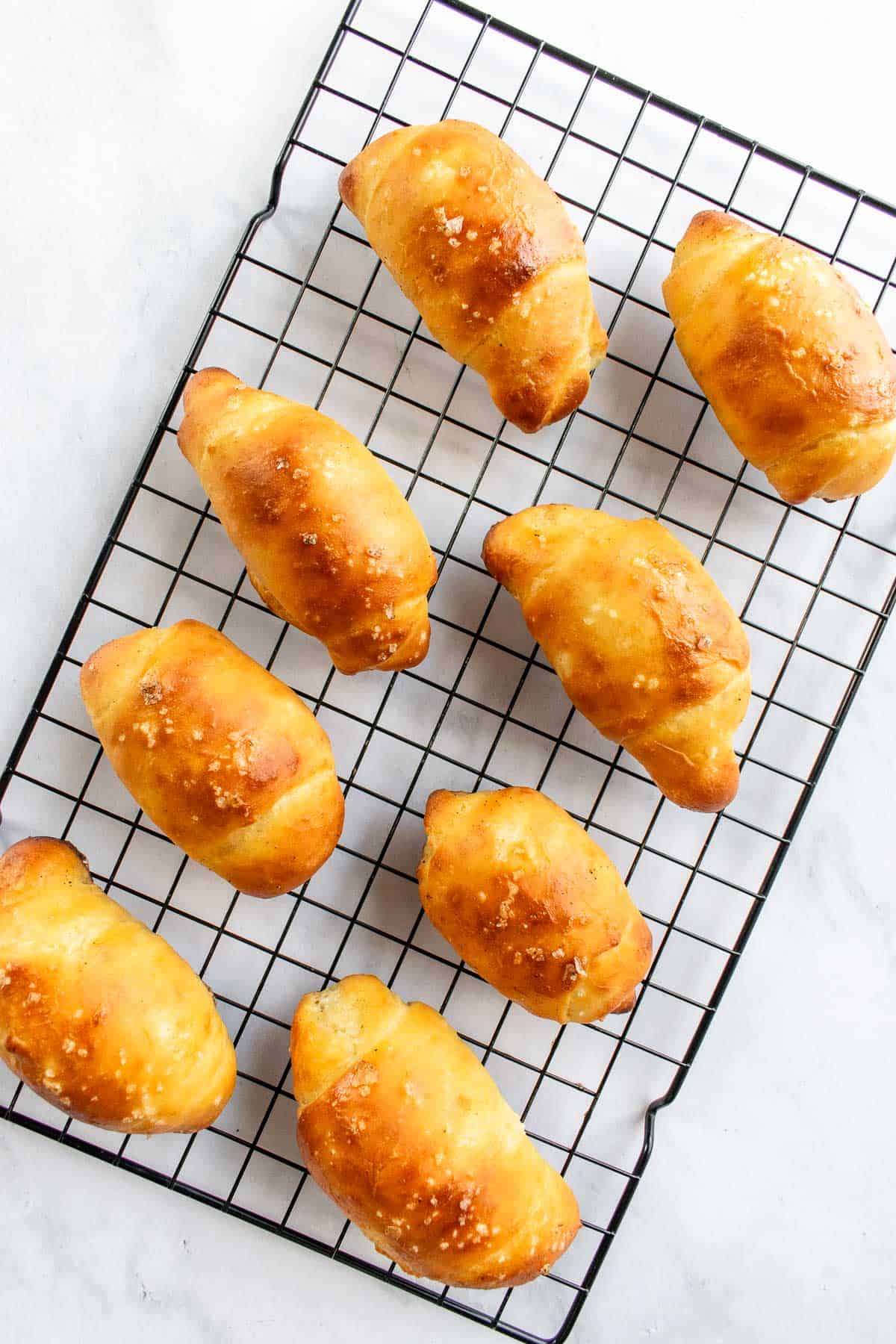 Eight golden bread rolls arranged on a wire cooling rack.