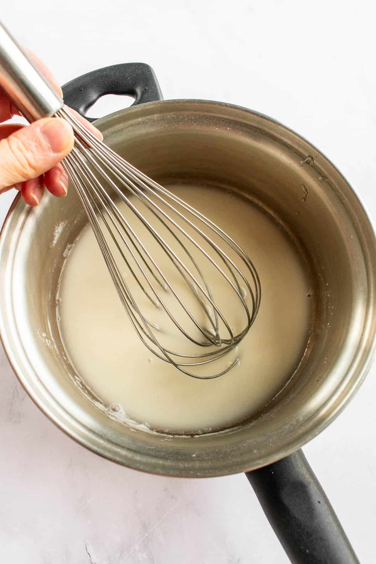 A hand whisking flour and water in a metal saucepan.