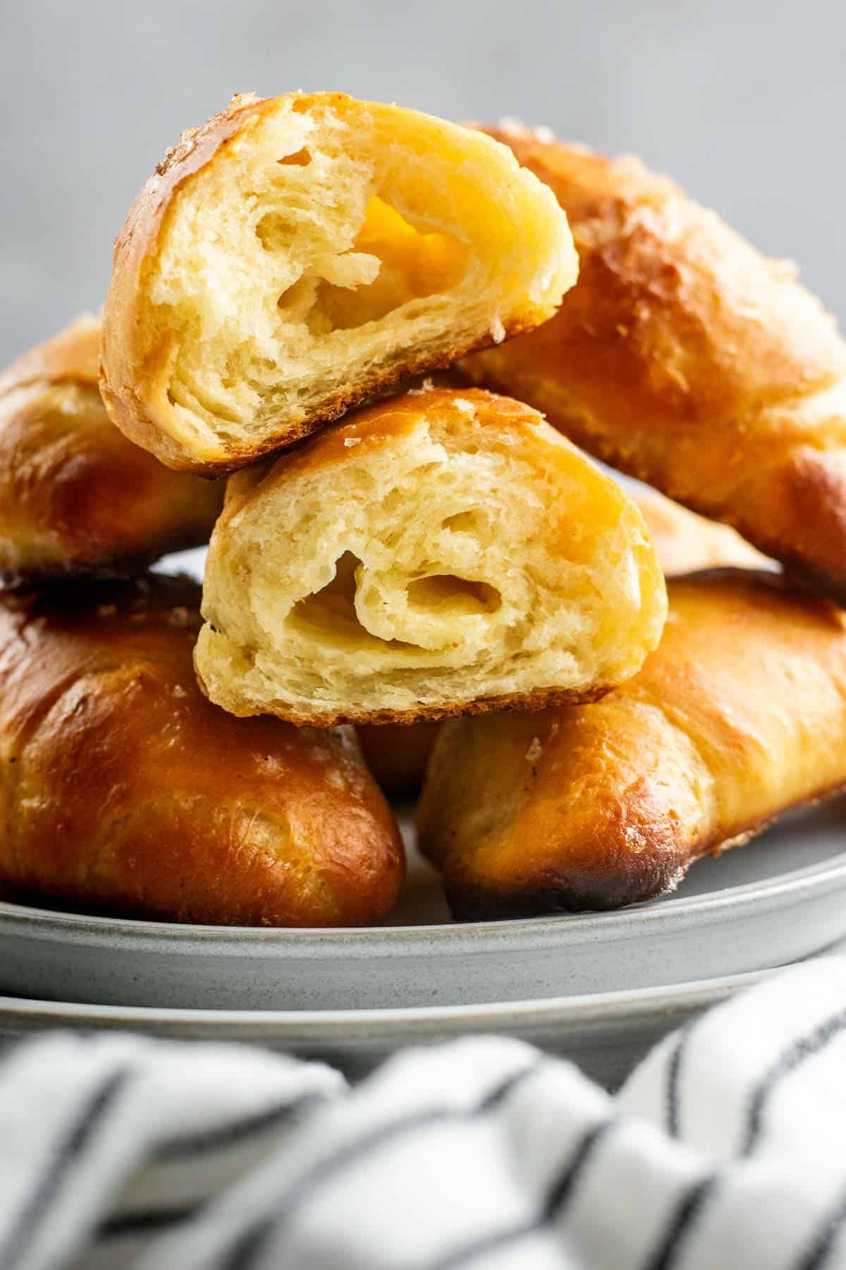 A bread bun torn in half to show the airy, fluffy interior on a plate with more baked buns.