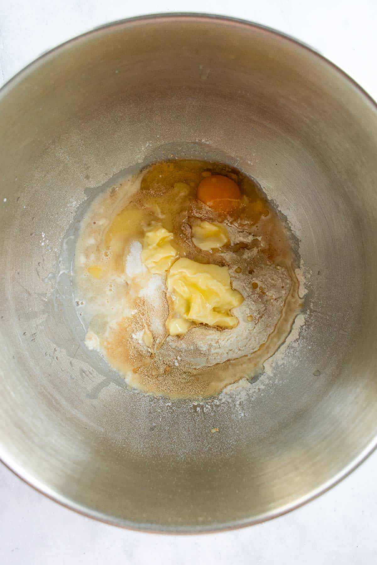 A large metal bowl filled with softened butter, sugar, salt, yeast, and an egg.