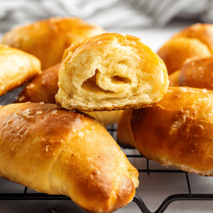 Half a dozen golden salt bread buns on a cooling rack, with one torn in half.