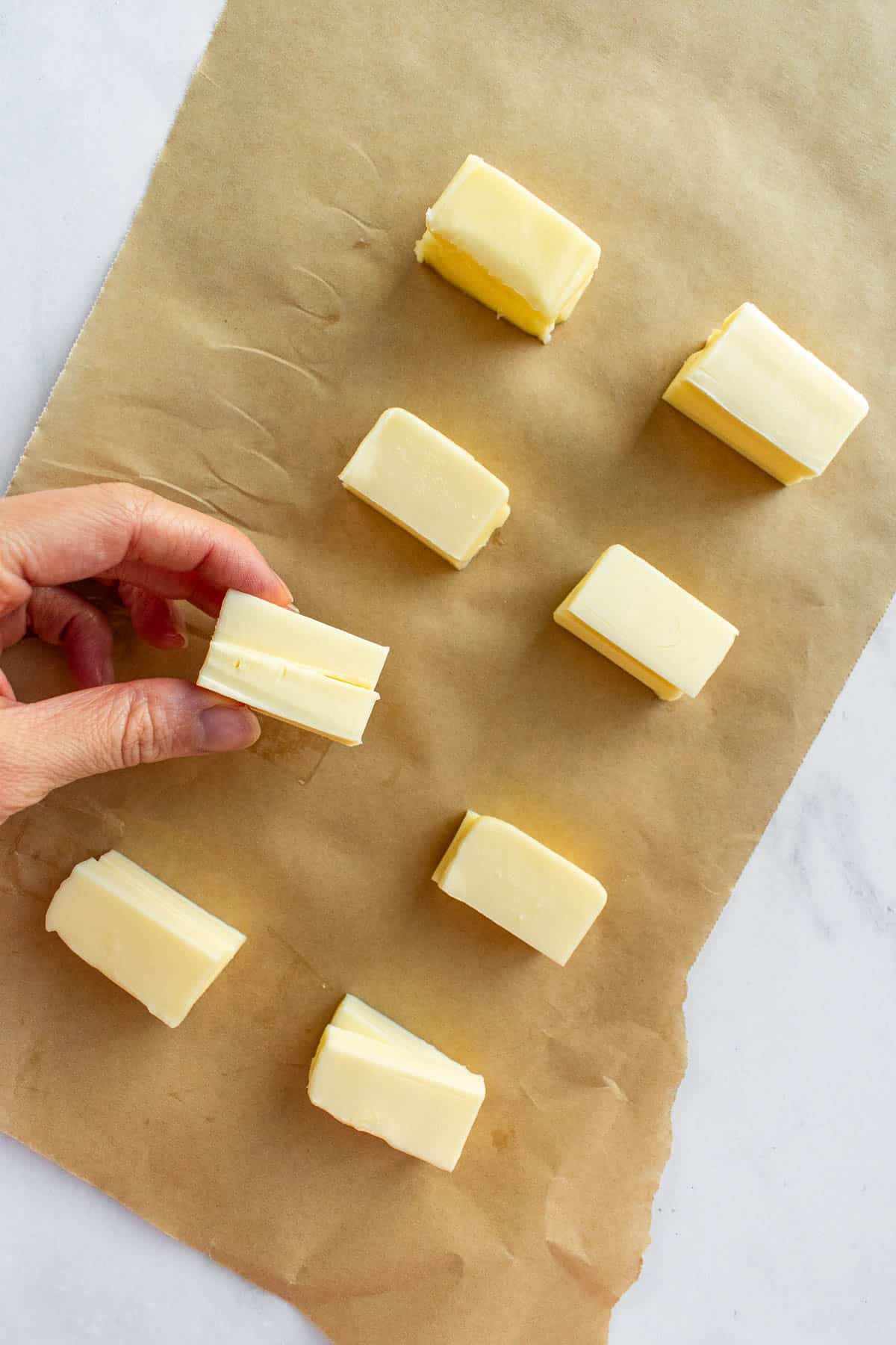 Eight small rectangles of butter arranged on a piece of brown parchment paper.