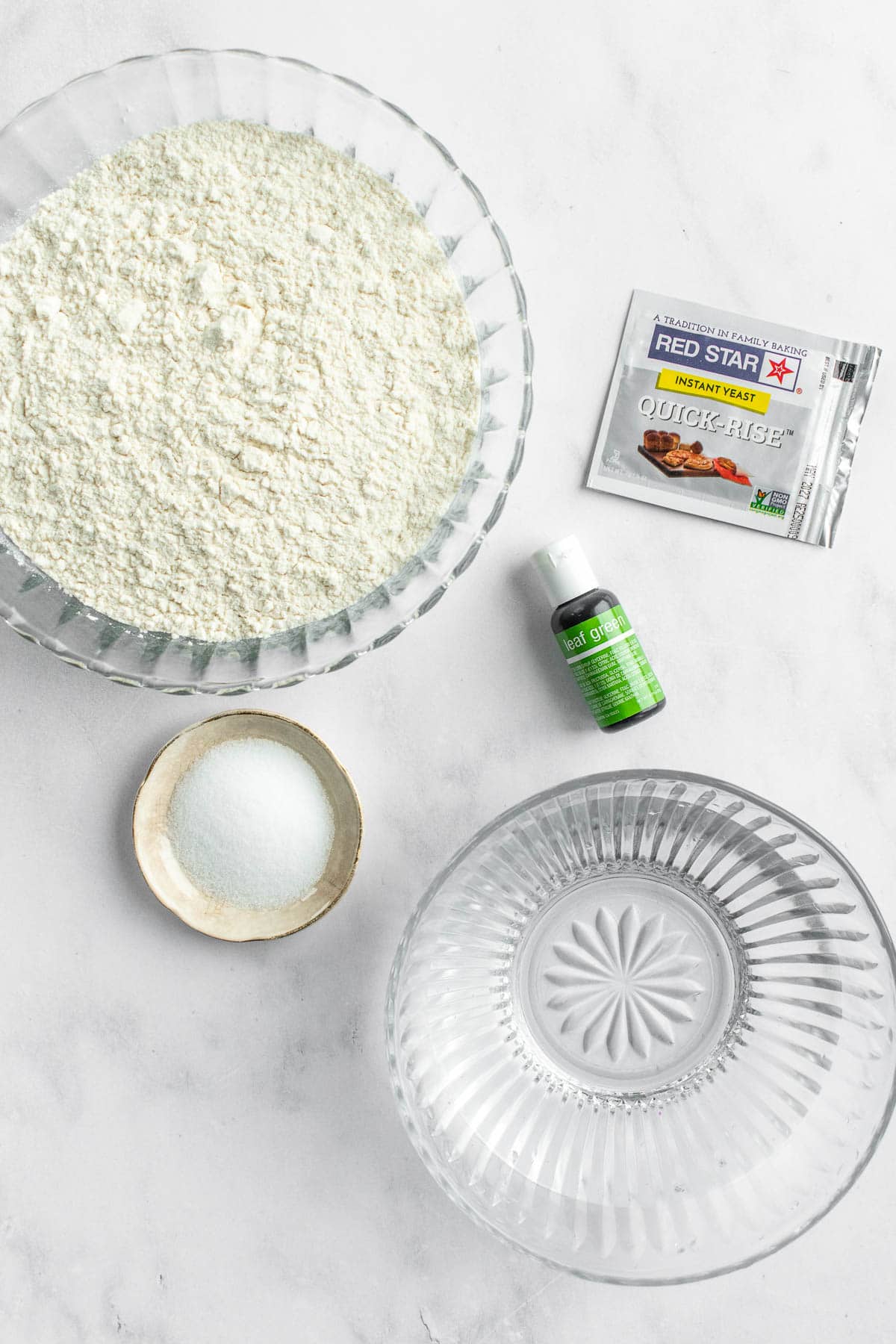 Bowls of water, flour, and salt next to a packet of yeast and a bottle of green food dye.