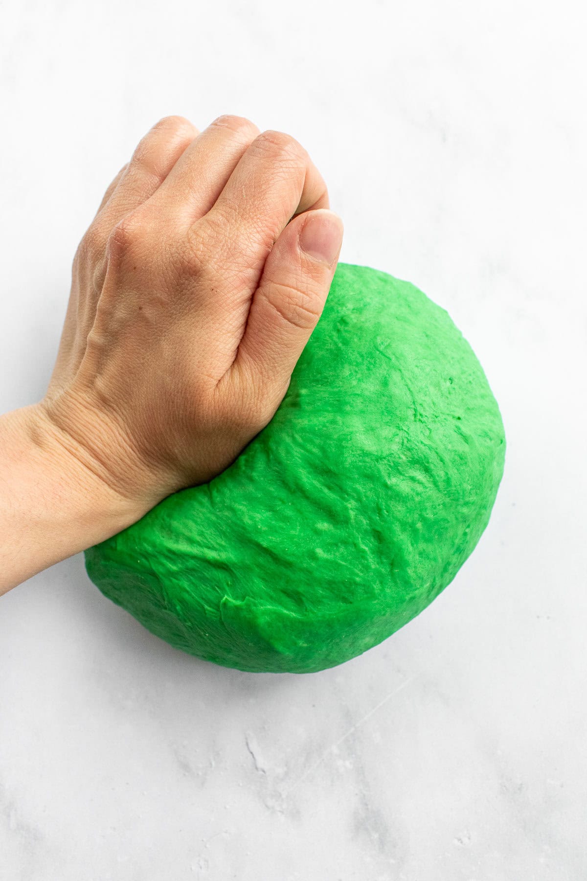 A hand kneading green bread dough on a marble surface.