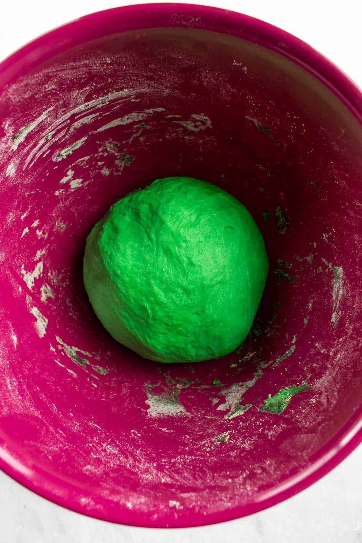 A small ball of green dough in a magenta mixing bowl.