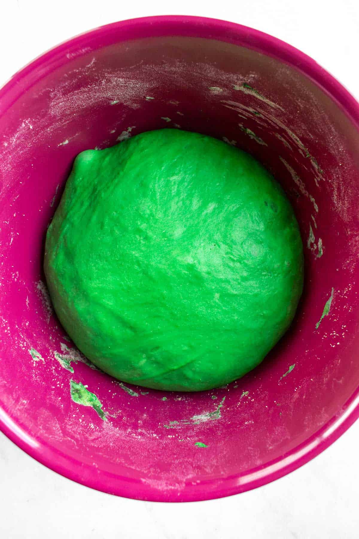 A large risen ball of green bread dough in a mixing bowl.