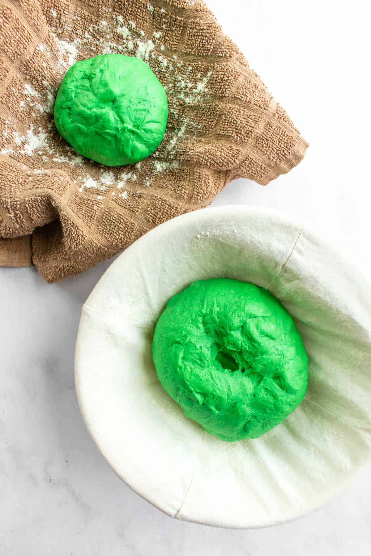 Two balls of bright green bread dough in proofing baskets on a light surface.