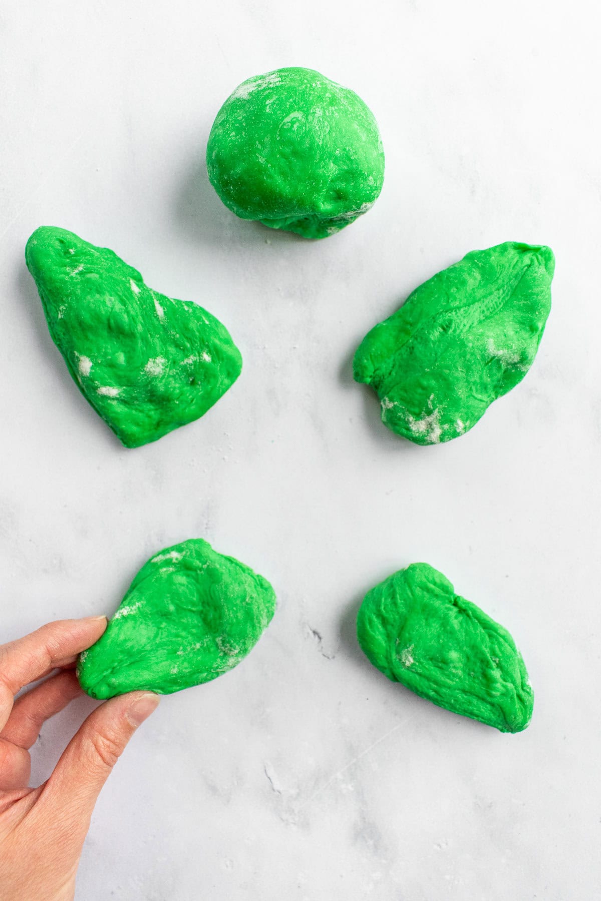 A hand shaping green bread dough into a ball and four thick triangles.