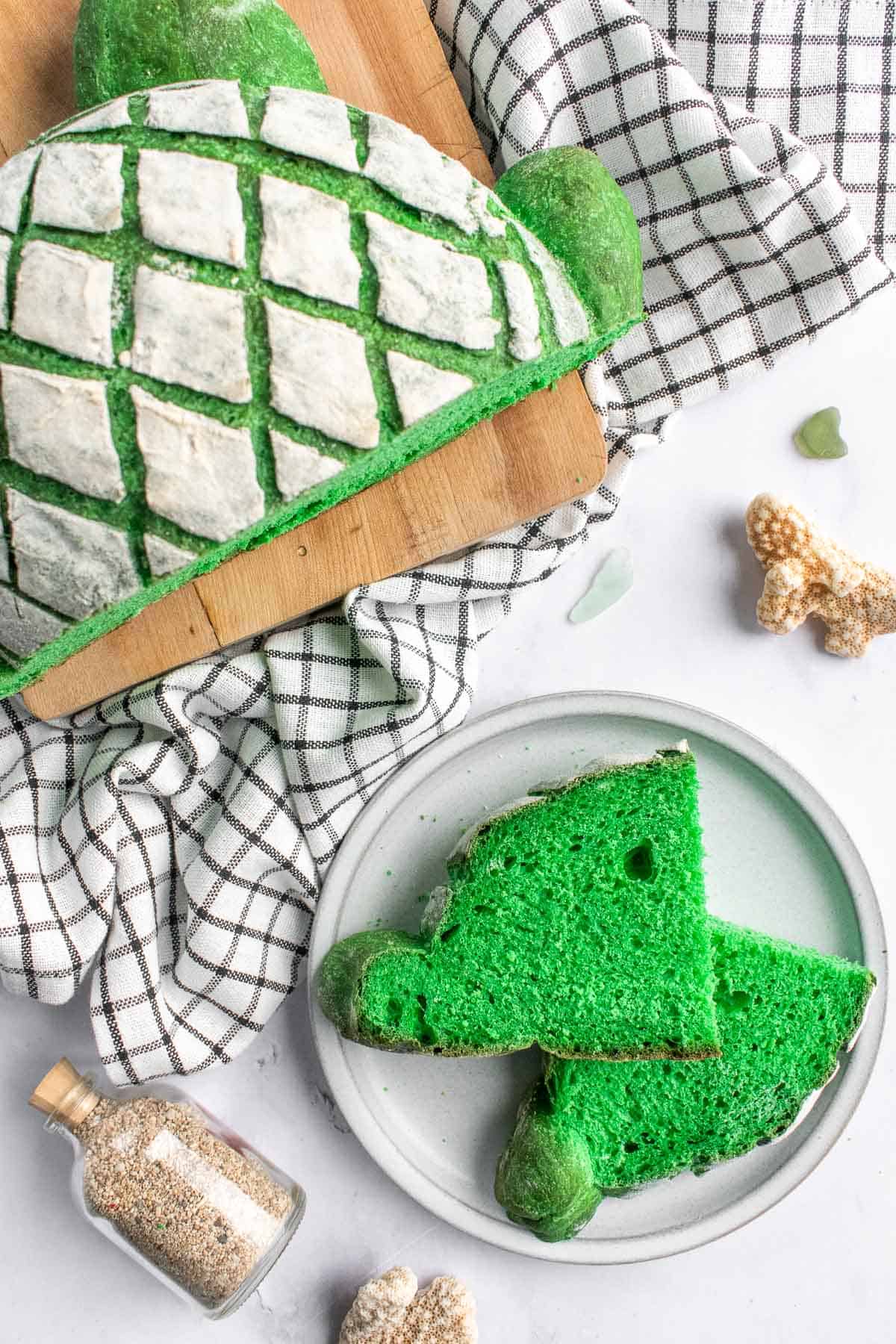 Two slices of green artisan bread next to a loaf scored with a cross-hatch pattern on a wooden board.
