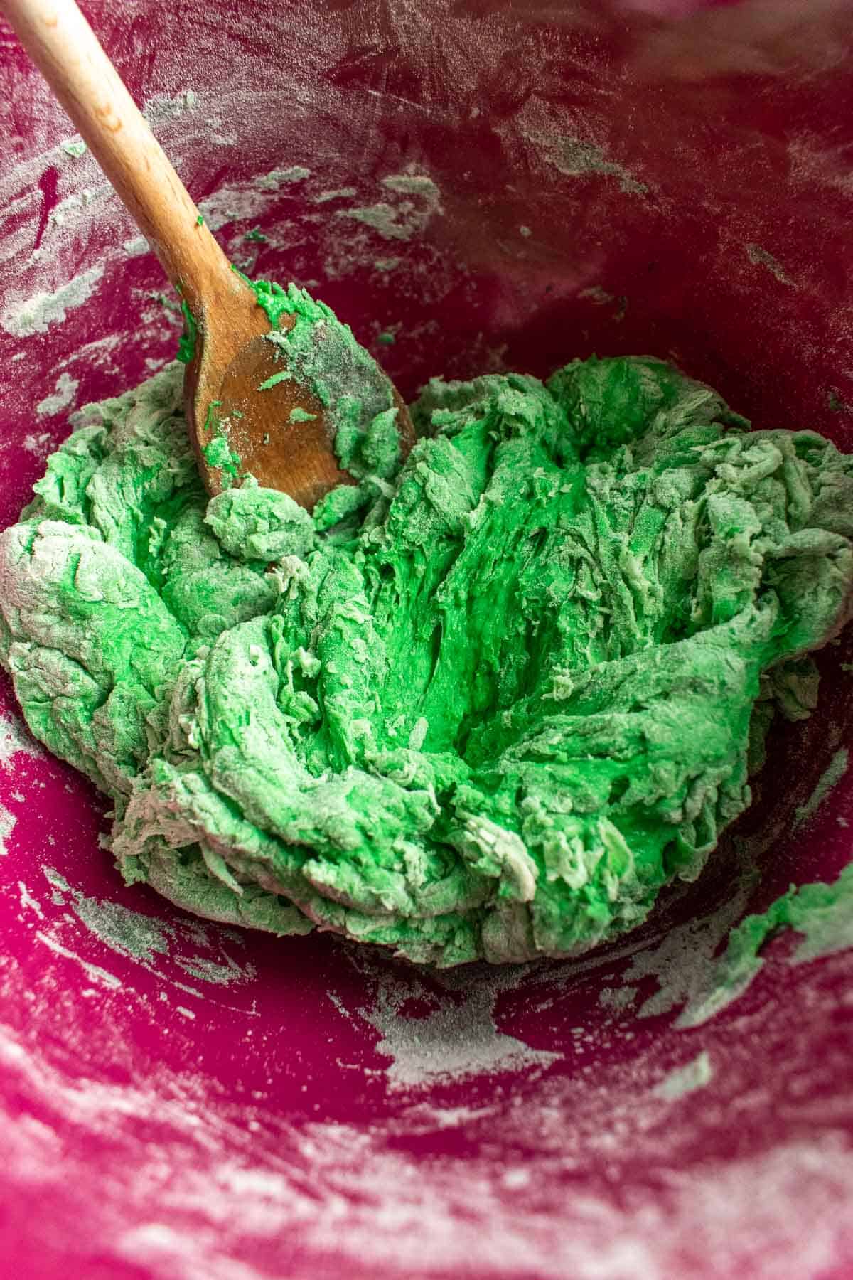 A shaggy green bread dough in a mixing bowl with a large wooden spoon.