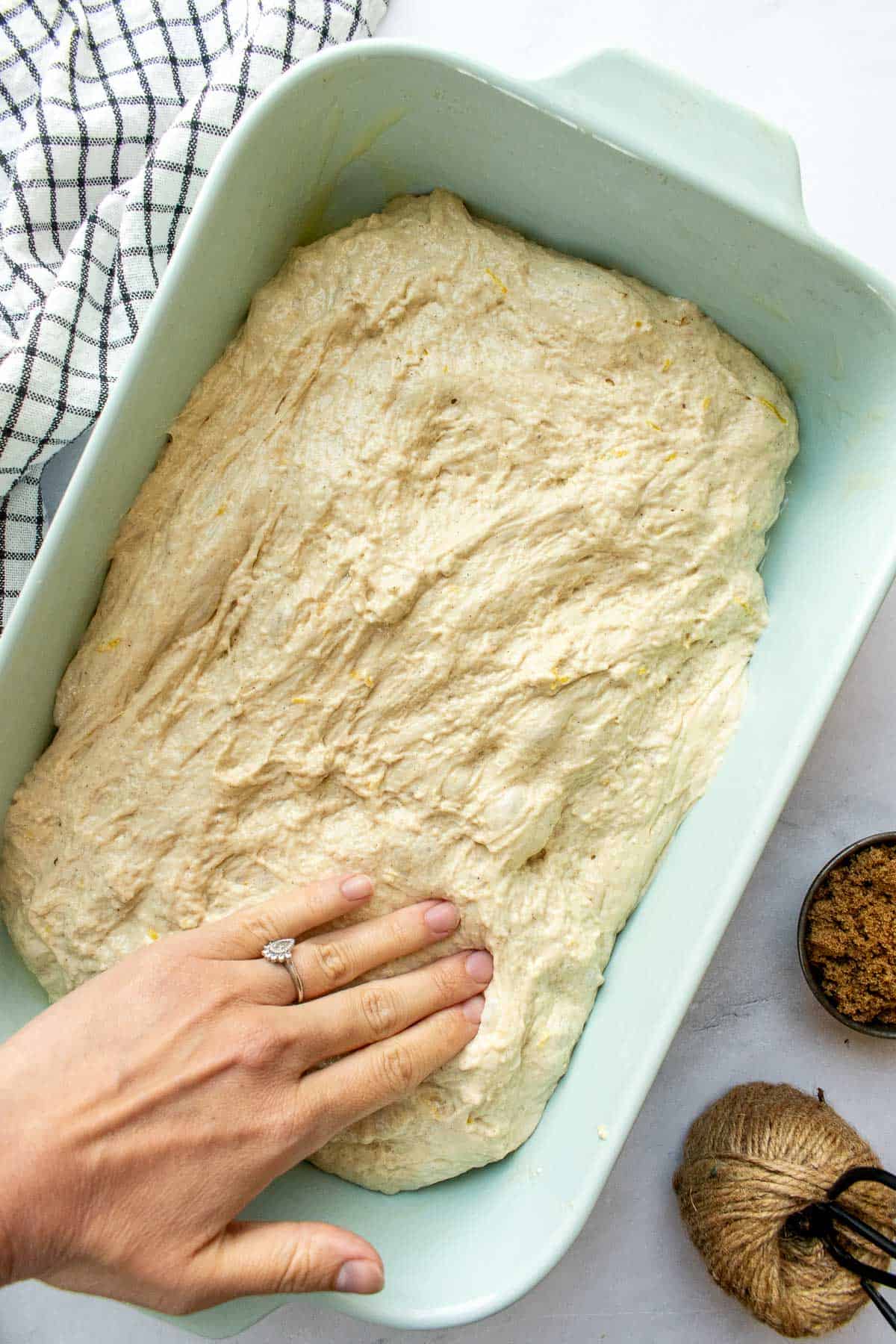 A hand pressing focaccia dough into a large blue baking dish.