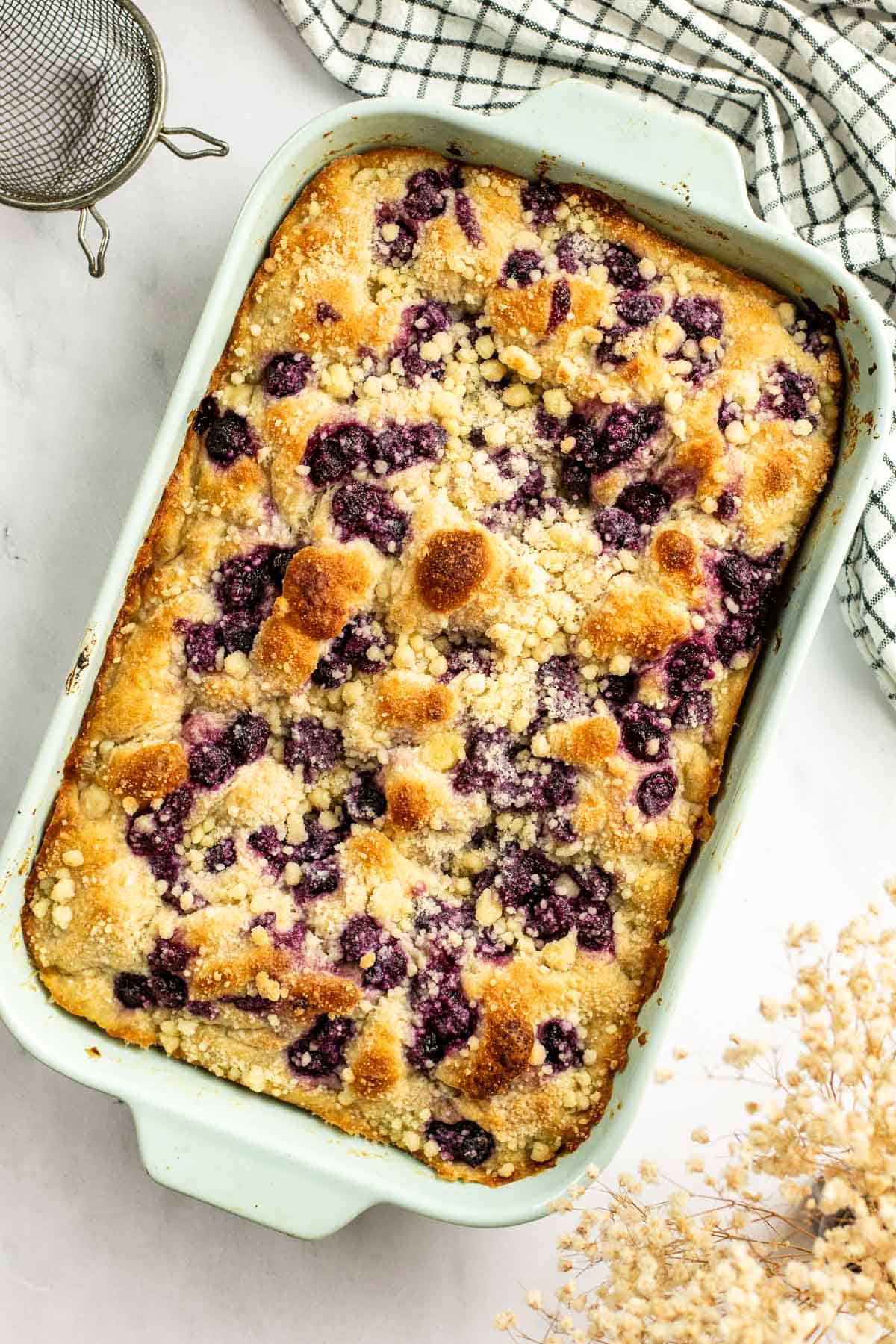Baked blueberry focaccia topped with streusel in a large baking dish on a light table.