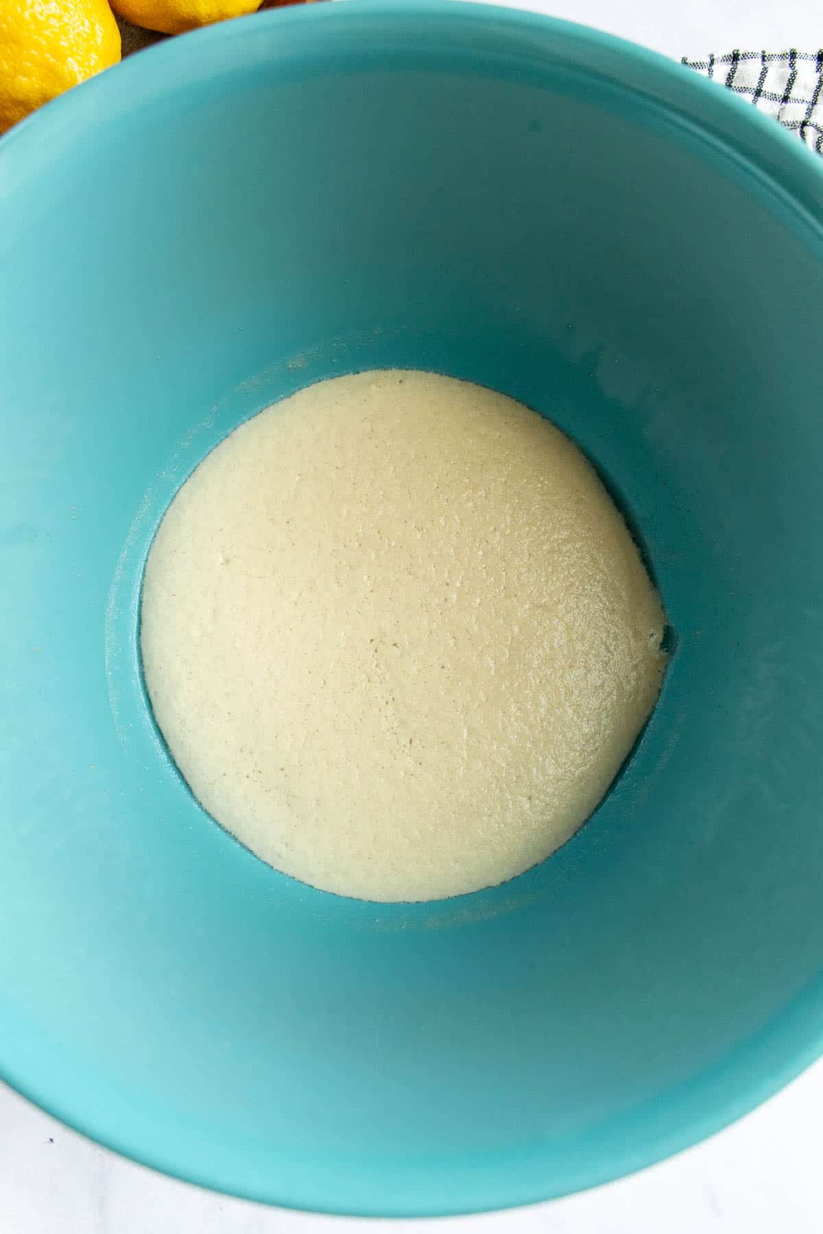 A blue mixing bowl filled with bubbly, activated yeast in water.