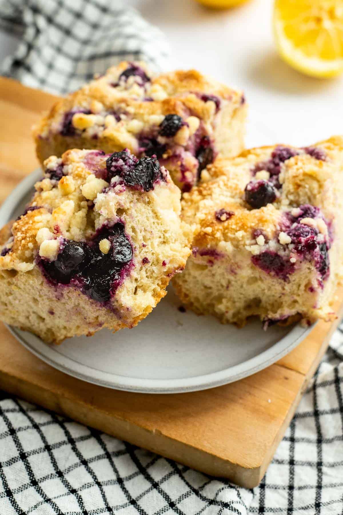 Three large squares of blueberry lemon focaccia stacked on a grey plate on a wooden board.