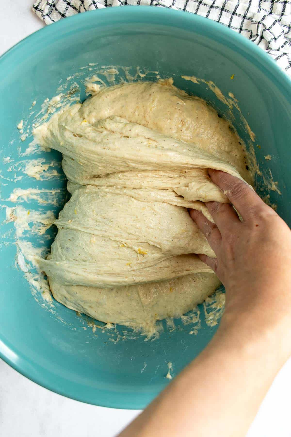 A hand folding focaccia bread dough over itself in a blue mixing bowl.
