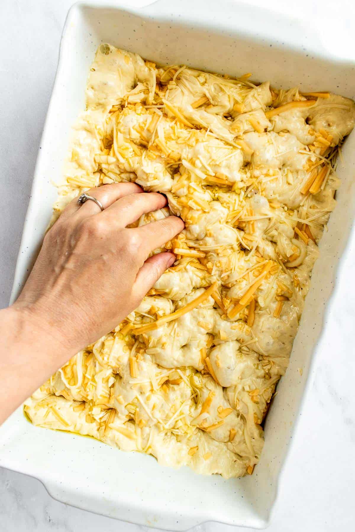 A hand dimpling focaccia dough to create dents on the surface.