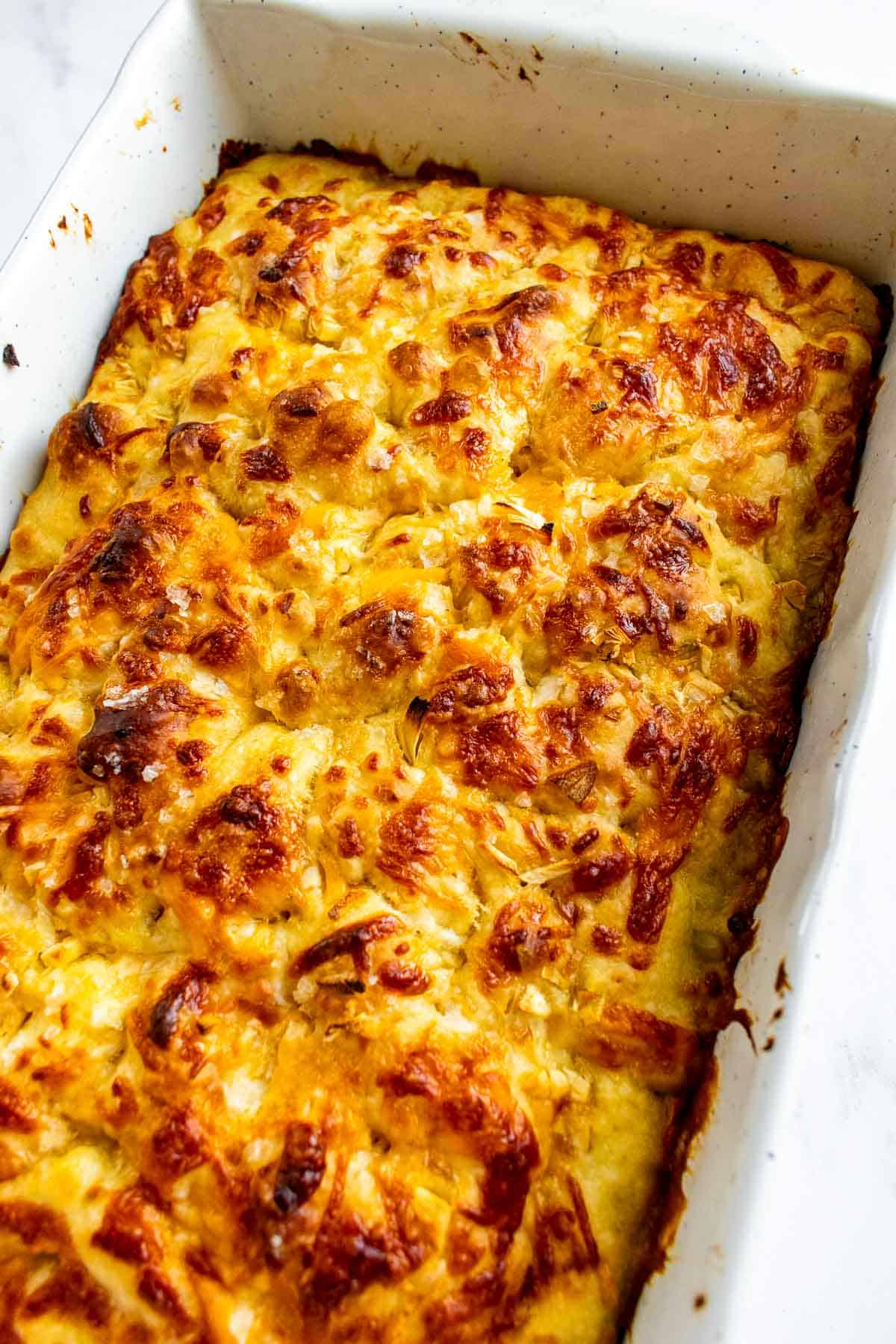 Golden cheese focaccia with a bumpy surface in a white baking dish.