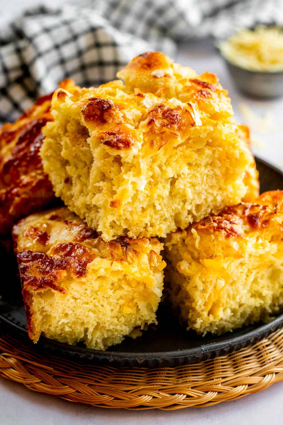 Three large square pieces of fluffy cheese focaccia piled on a metal plate.