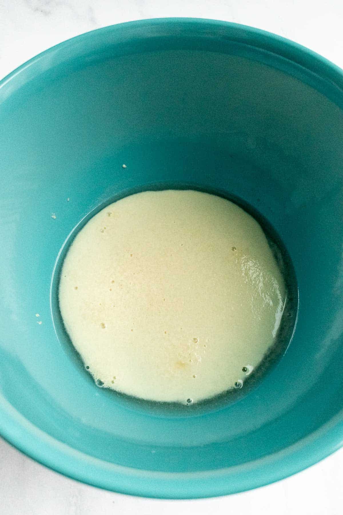 A blue bowl filled with bubbly active dry yeast in water.