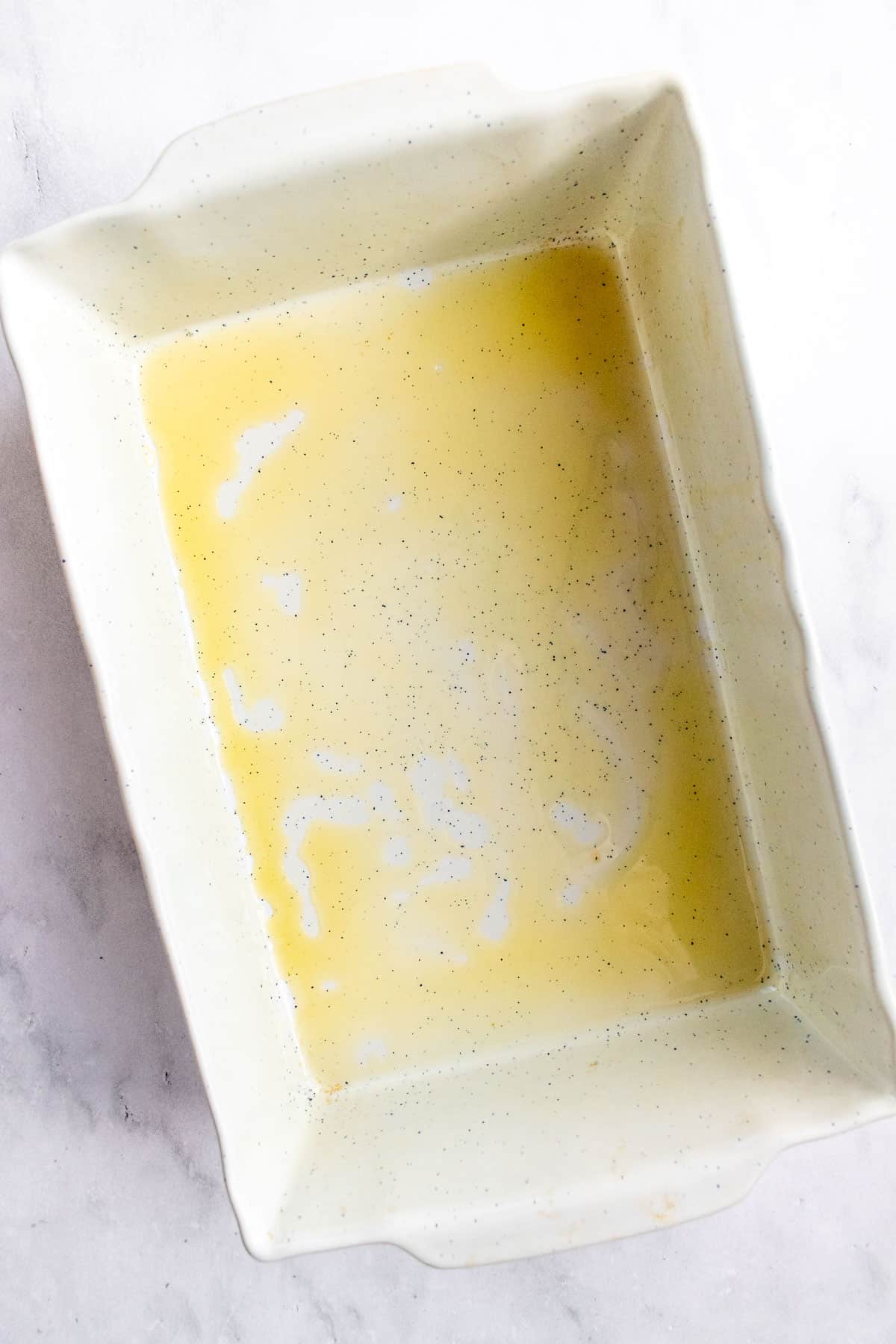A white baking dish with the bottom covered in olive oil.