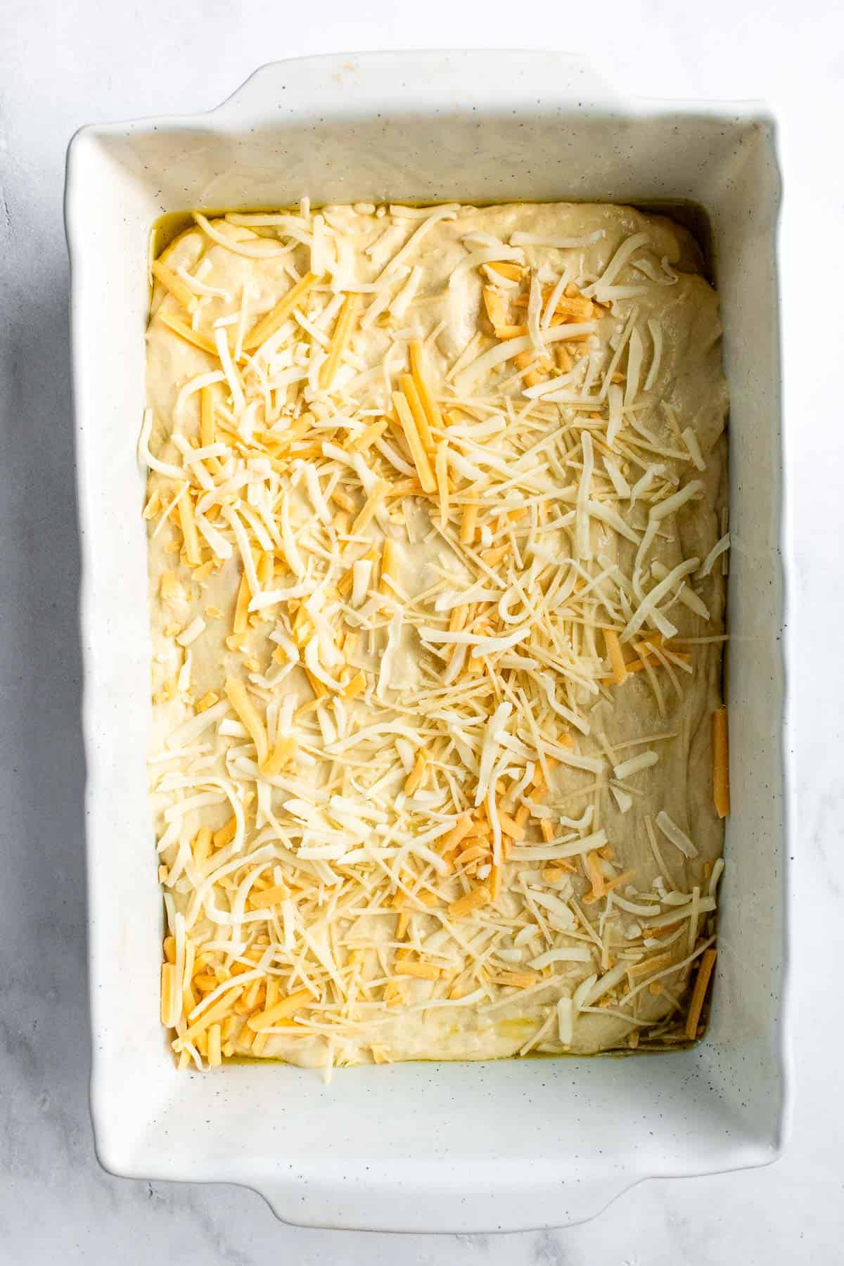 Bread dough spread in a baking dish and topped with shredded cheese.
