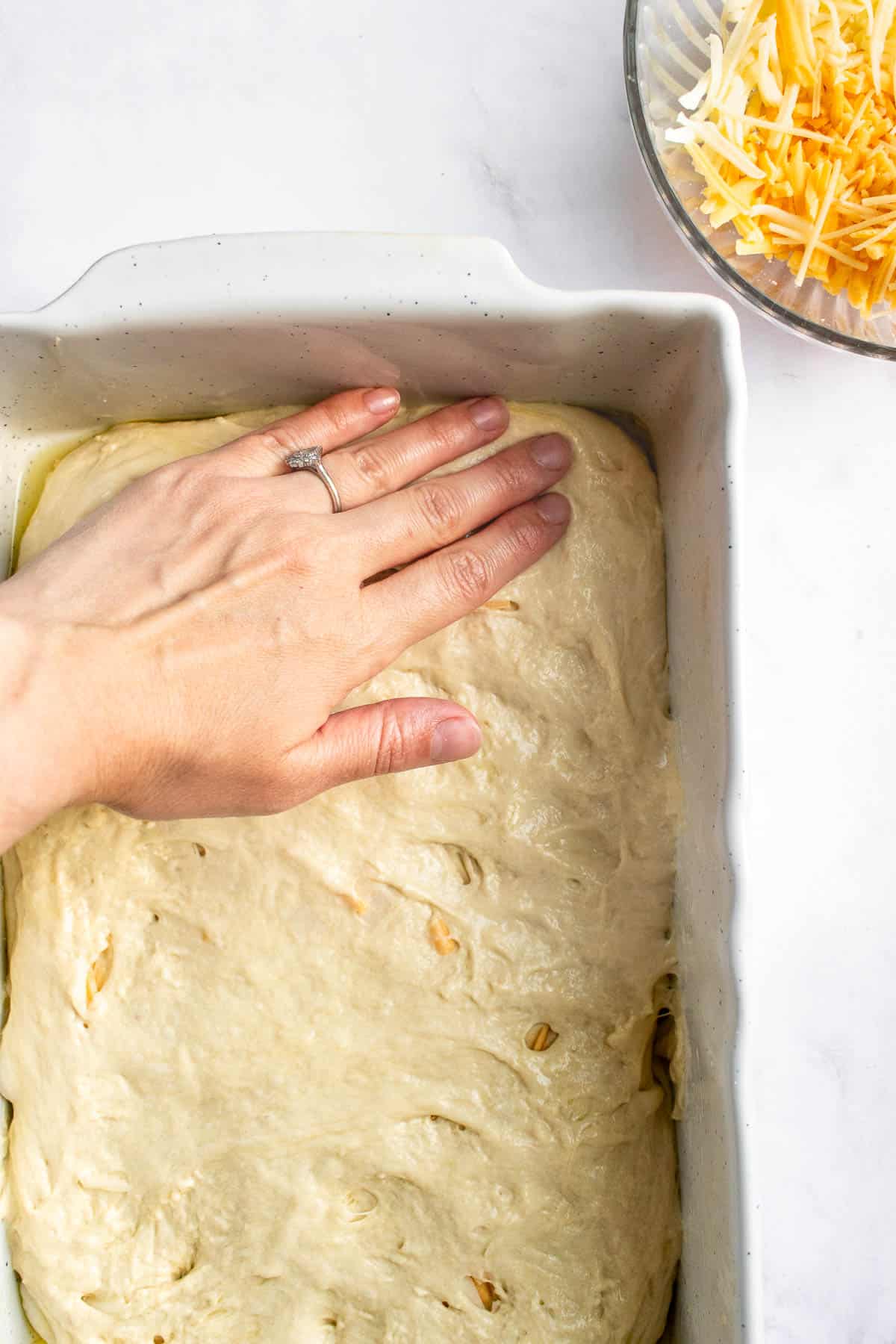 A hand pressing focaccia dough into a baking dish.