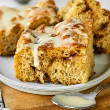 Three slices of cinnamon roll focaccia on a small plate topped with white glaze.