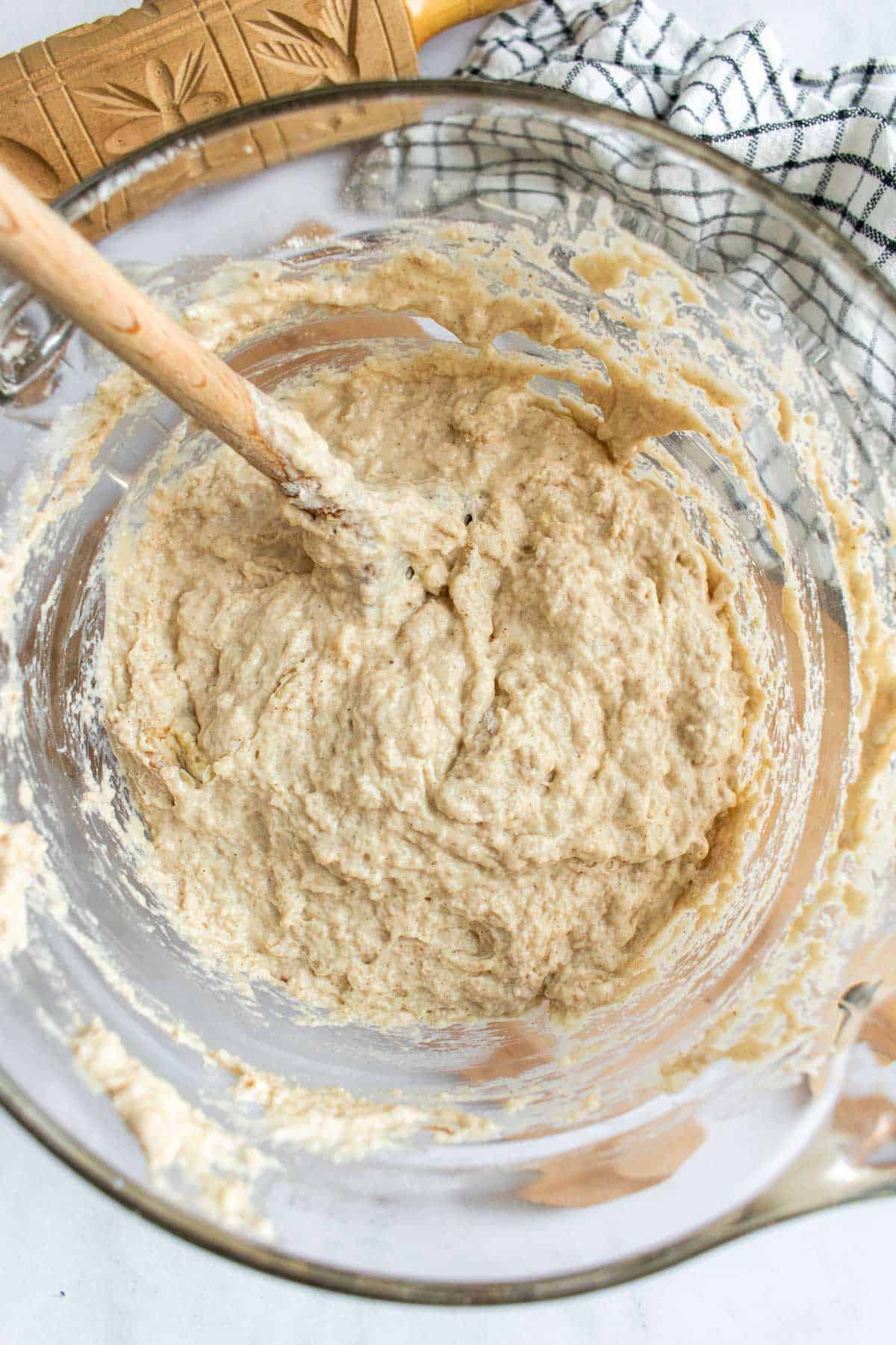 Wet focaccia dough in a mixing bowl with a wooden spoon stuck in it.